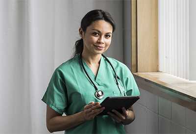 A healthcare professional in scrubs holding a tablet
