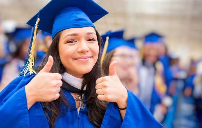 A woman wearing a cap and gown smiles and gives a thumbs-up.
