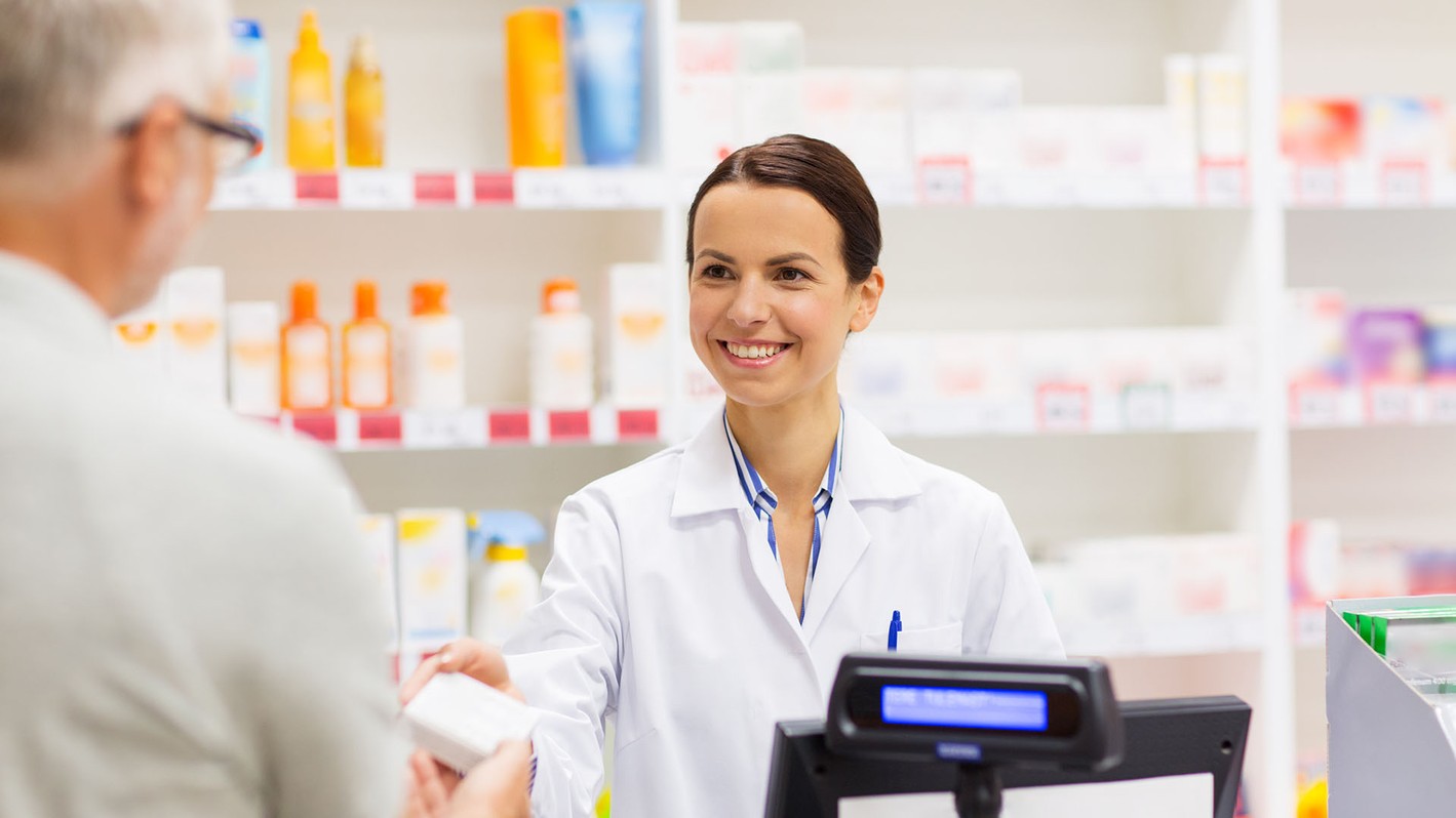 Image of a pharmacy technician smiling while assisting a customer.