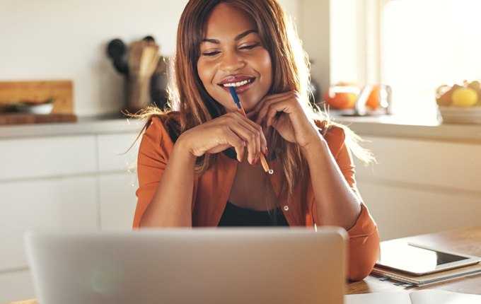 A woman smiles while looking at a computer screen.