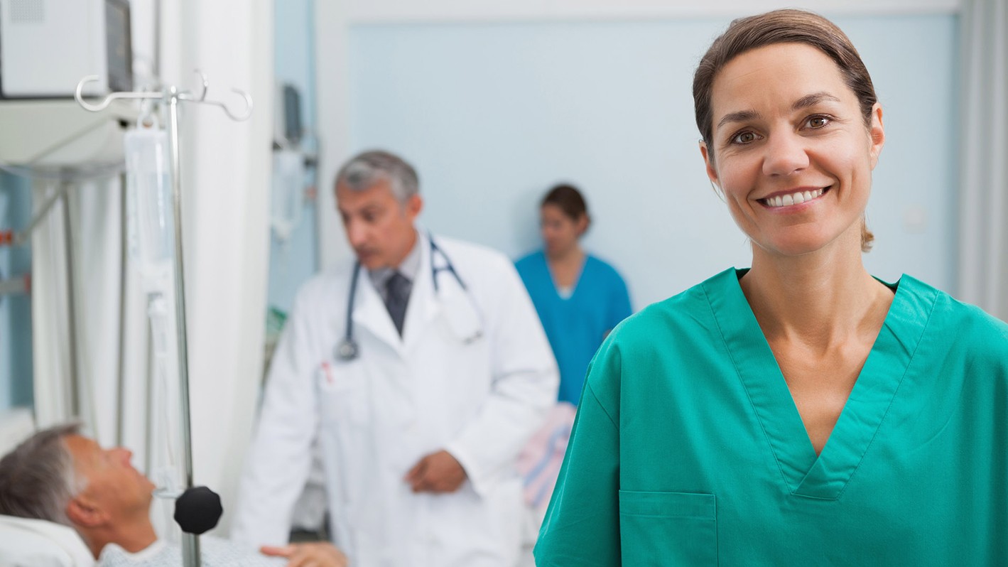 Image of a patient care technician smiling with other heqalthcare professionals in the background.